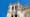 Façade sculptée d’une cathédrale gothique vue en contre-plongée, avec tours, arcs, rosace et gargouilles sous un ciel bleu.