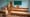 Salle de classe vide avec rangées de bureaux et chaises en bois, tableau vert et pupitre de professeur devant un mur bleu clair.
